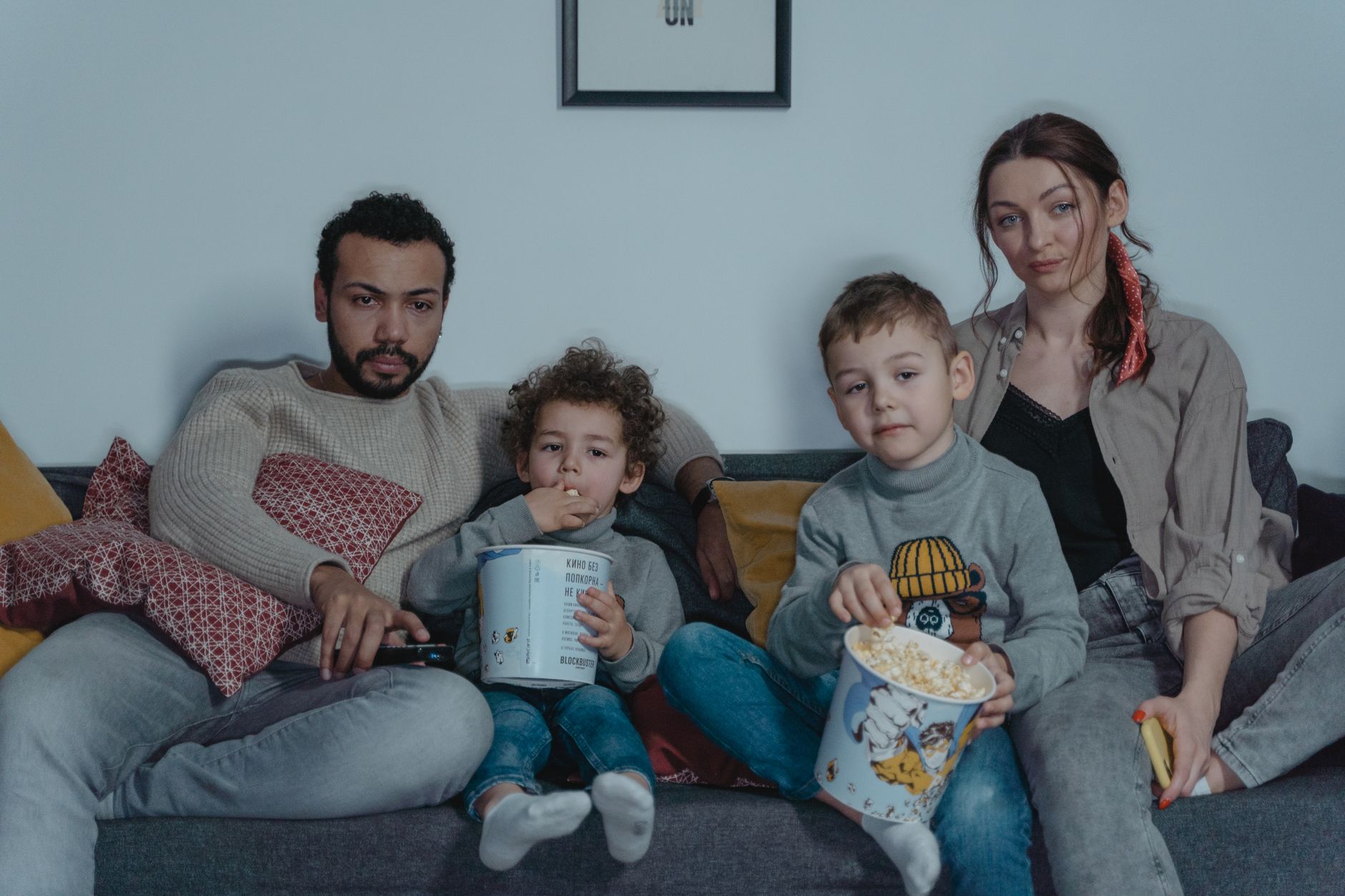 Famille de quatre personnes profitant d'une soirée cinéma confortable avec du pop-corn sur le canapé.