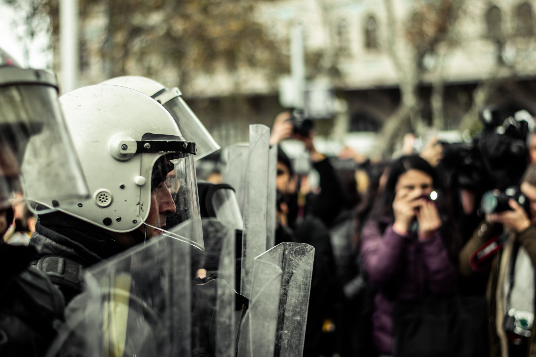 Des policiers casqués et boucliers confrontés par une foule de photographes.