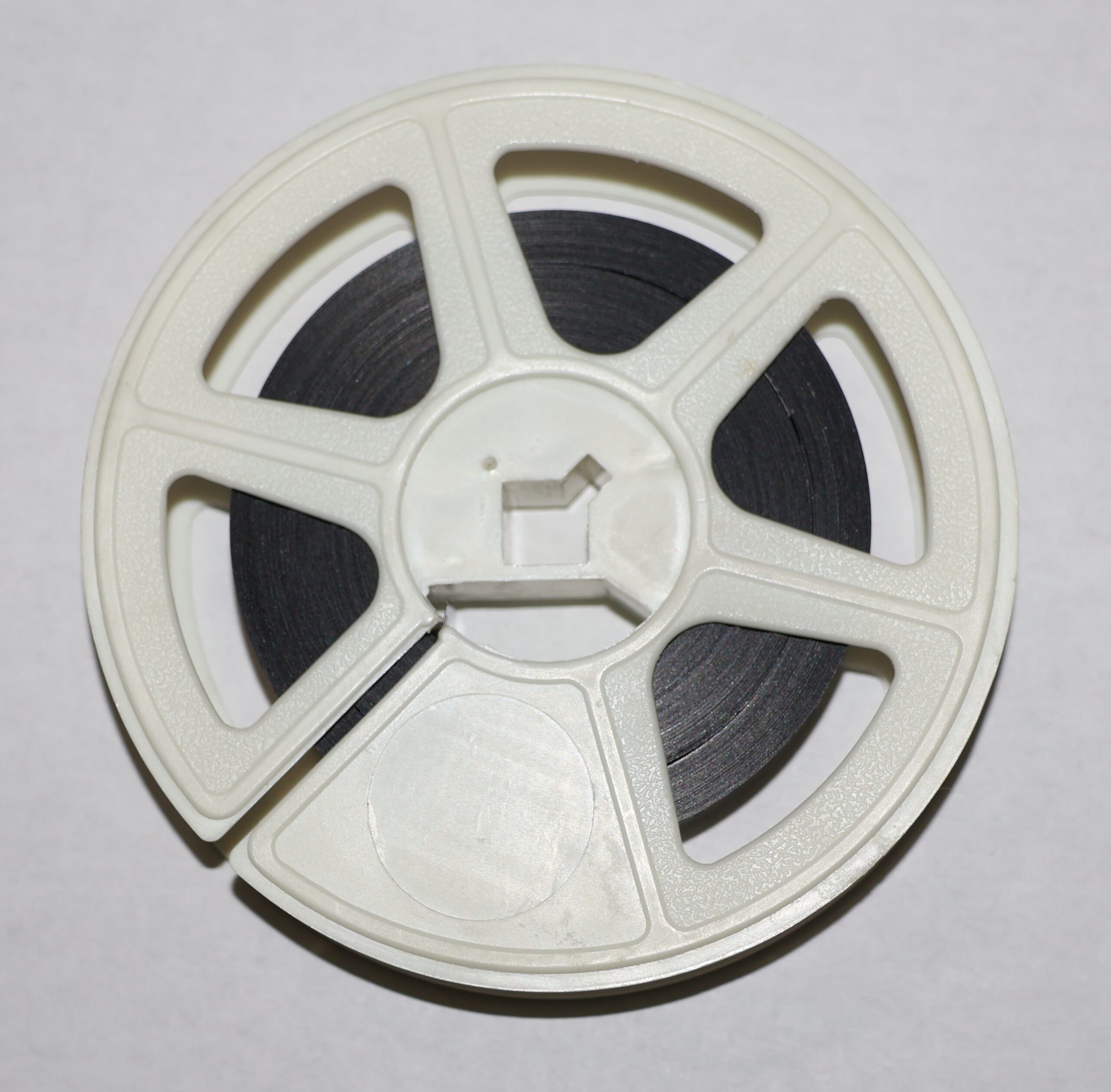 Bobine de film en plastique clair avec pellicule sombre enroulée, vue de dessus sur fond gris uni.
